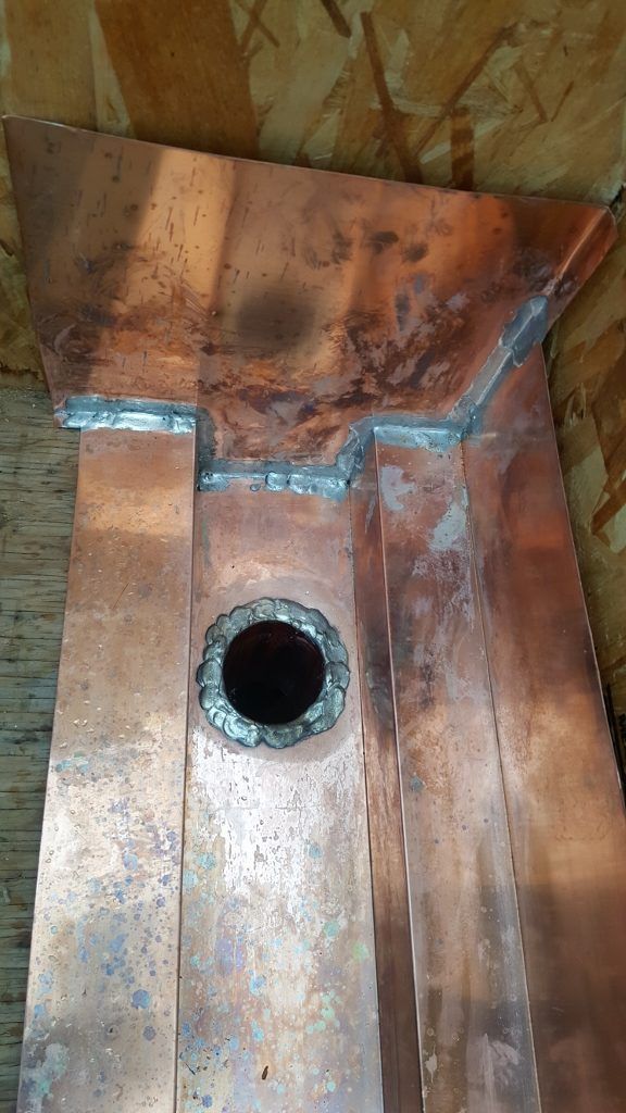 Copper gutter with a drain, showing solder joints and patina.