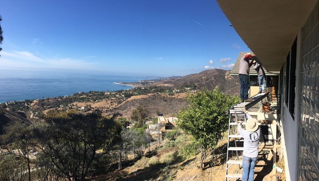 People working on a building's exterior with a scenic ocean and mountain view.