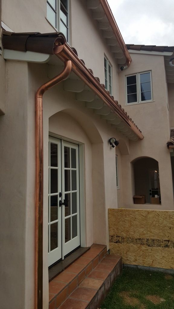 Copper gutters on a beige stucco house with French doors and a tile roof.