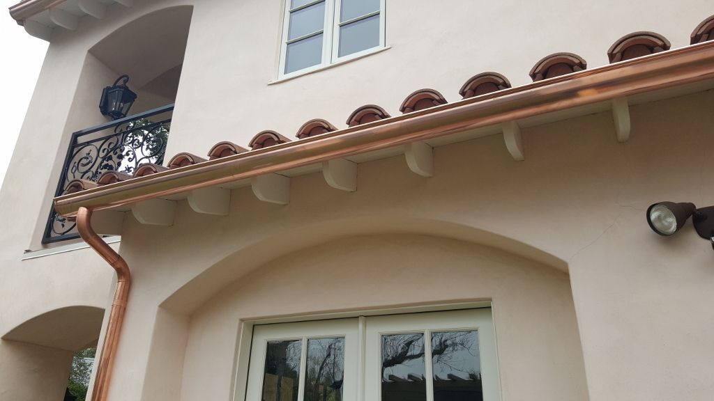 Copper rain gutters on a stucco home with an arched window and balcony.