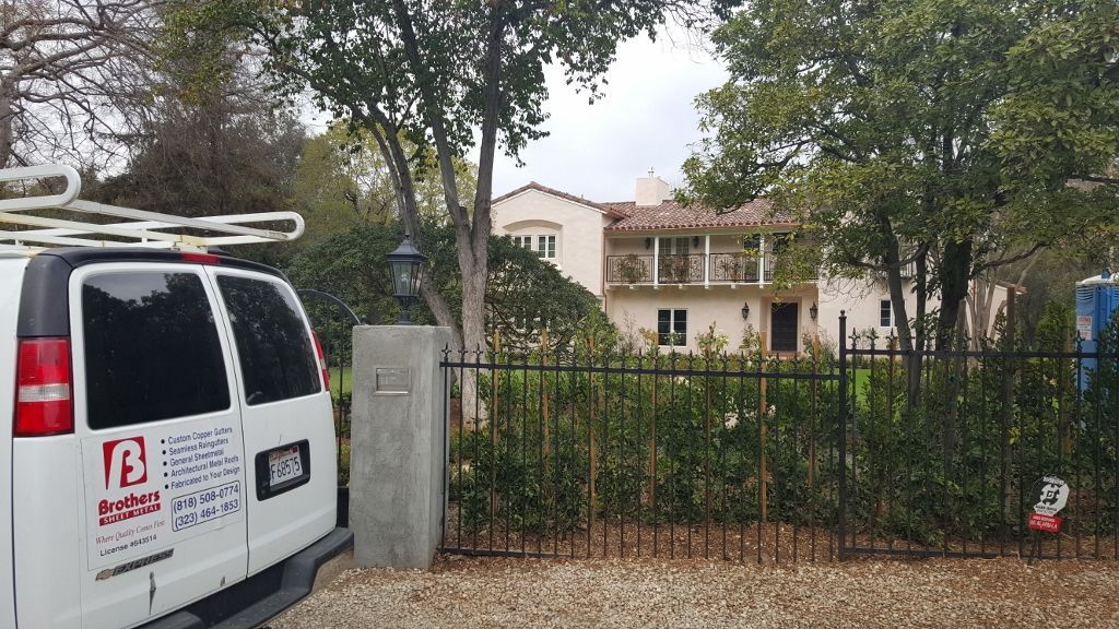 White van in front of a two-story house with a balcony, behind a fence and bushes.