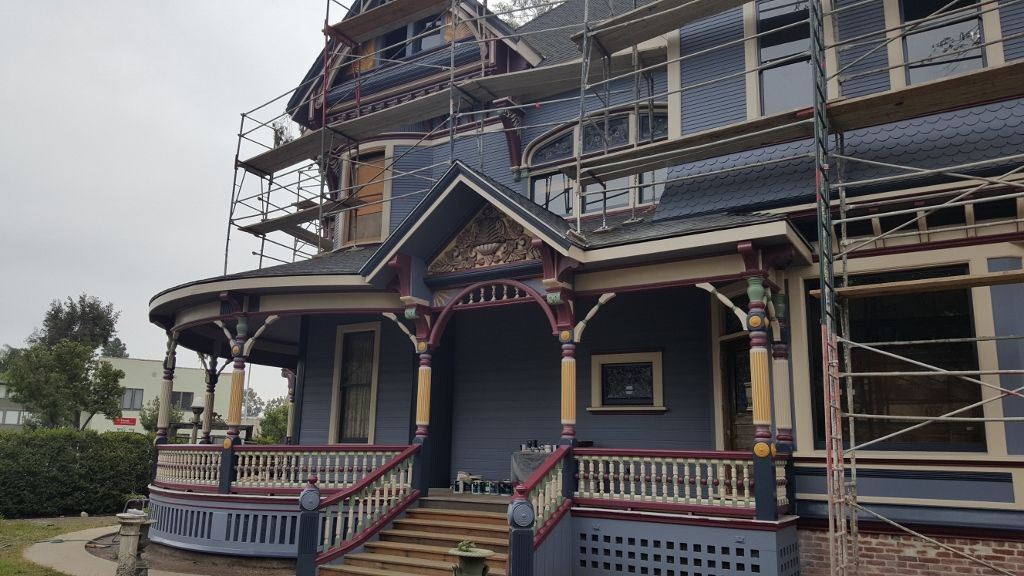 Victorian house with scaffolding during renovation, painted dark blue with ornate details, overcast day.