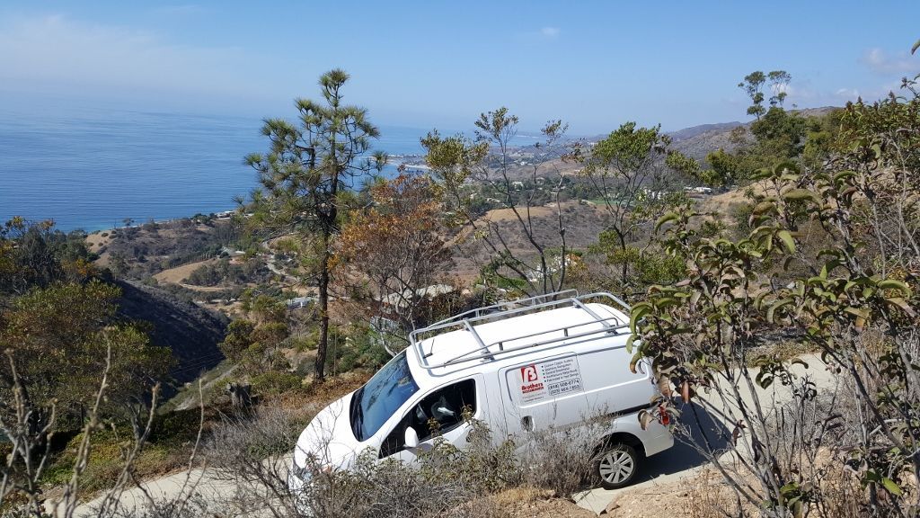 White van on a hillside road with ocean view in the background.
