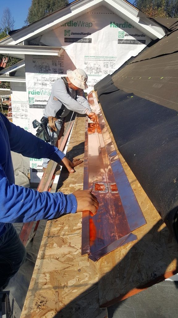 Two workers installing copper flashing on a roof.