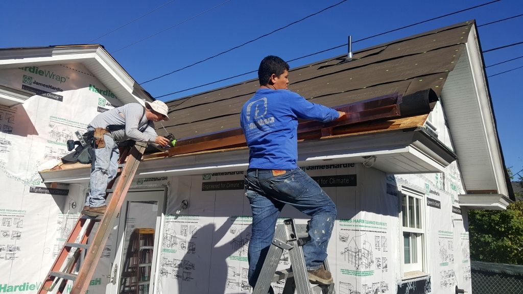 Two construction workers on ladders installing roofing on a house on a sunny day.