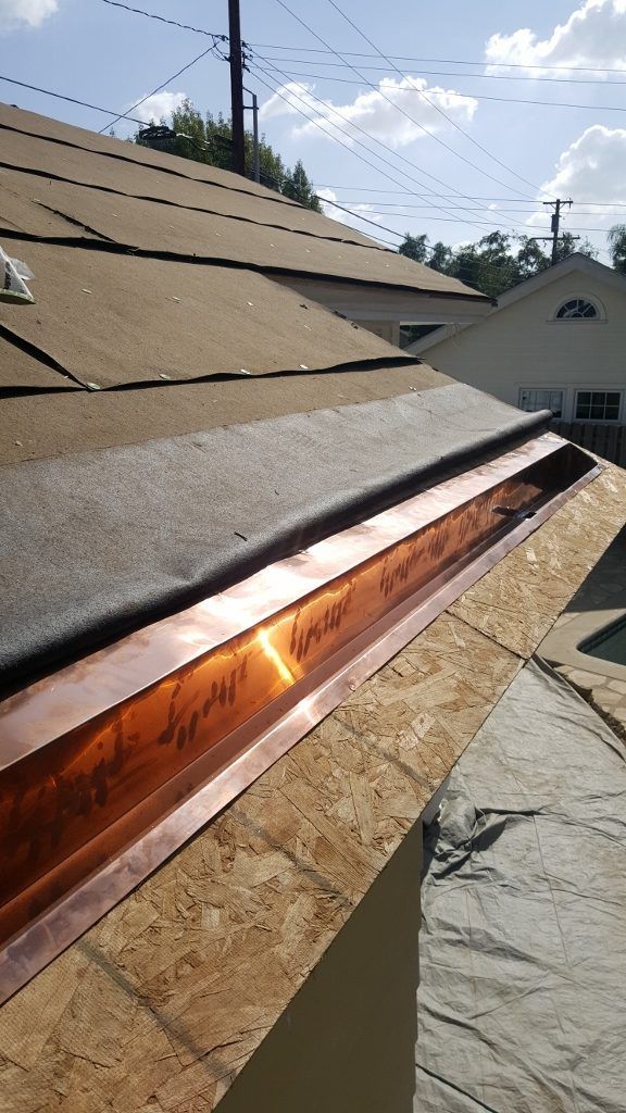 Copper flashing installed on a roof, partially covered with black roofing material, under a blue sky.
