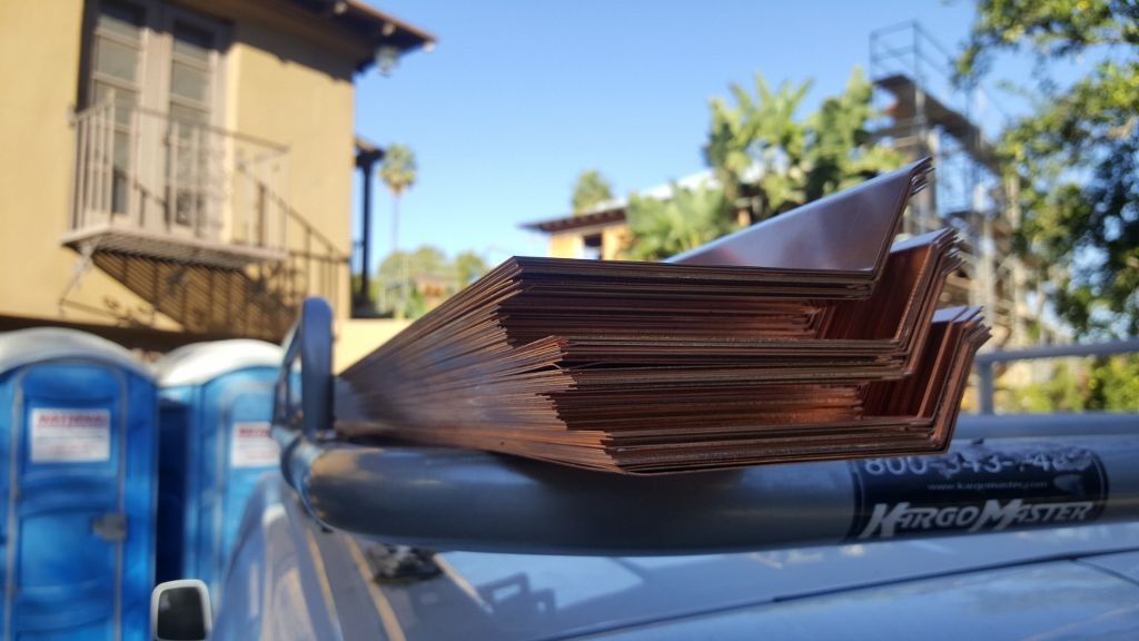 Copper flashing stacked on a truck rack, with portable toilets in the background. Sunny day.