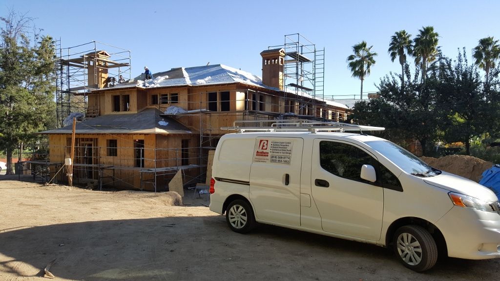 A white work van parked in front of a house under construction on a sunny day.