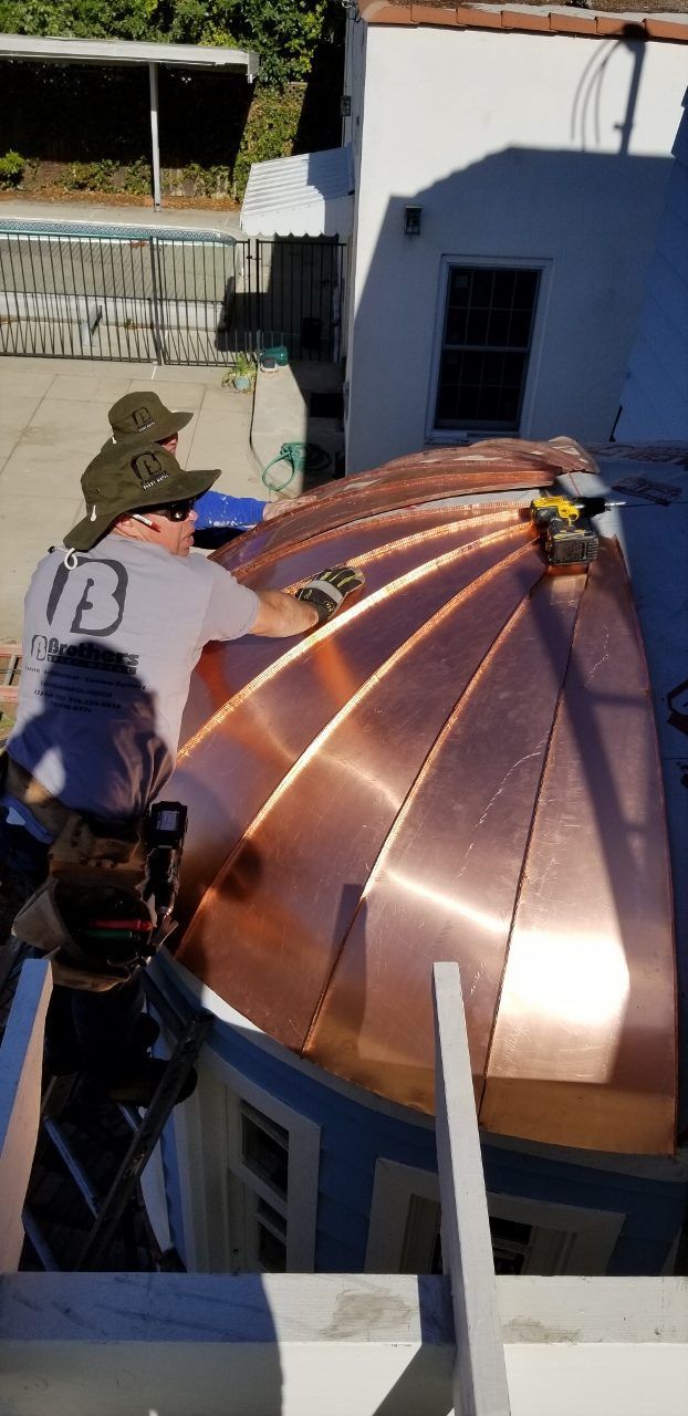 Men installing copper roofing on a structure outdoors.