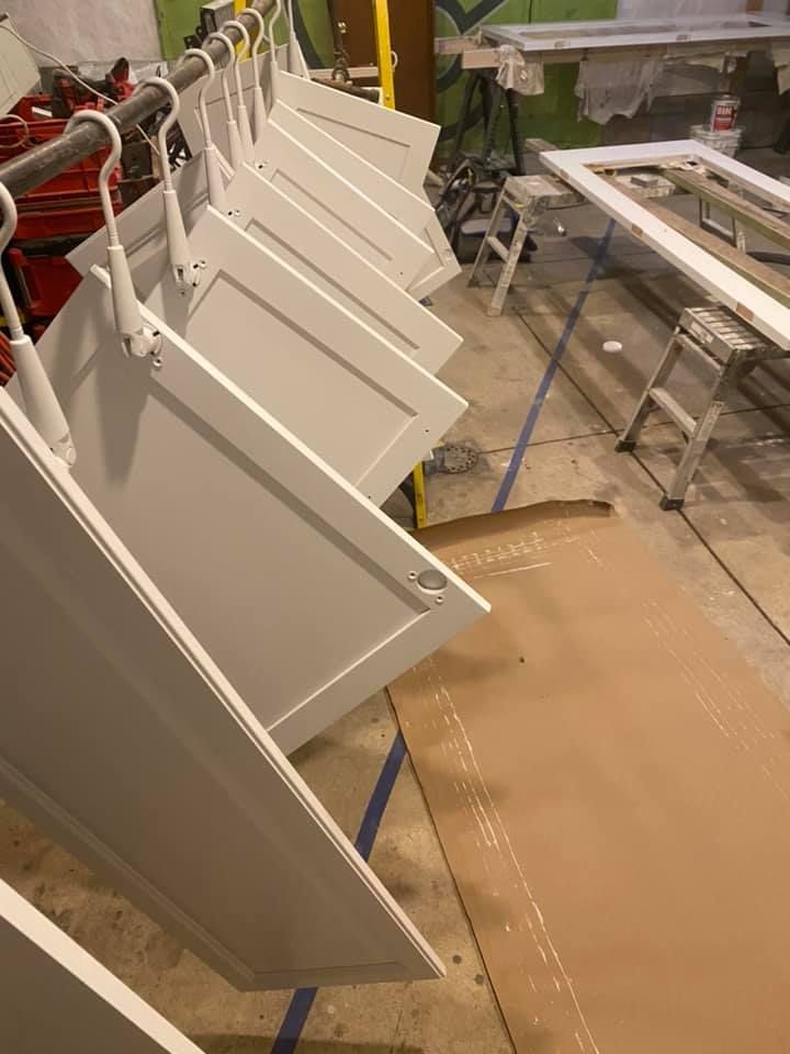 A row of white cabinet doors hanging on hooks in a room.