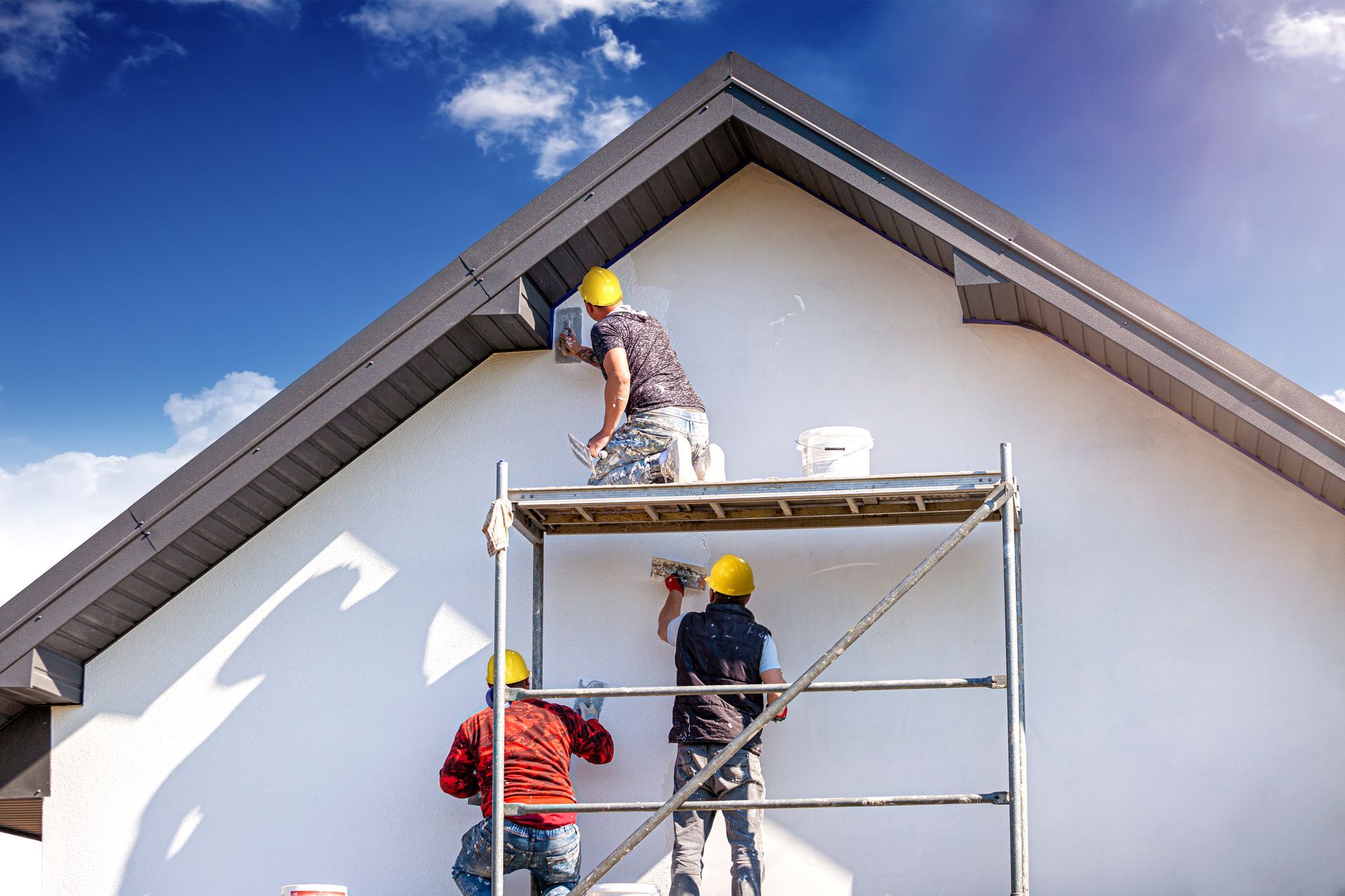 Two men are painting the side of a house on a scaffolding.