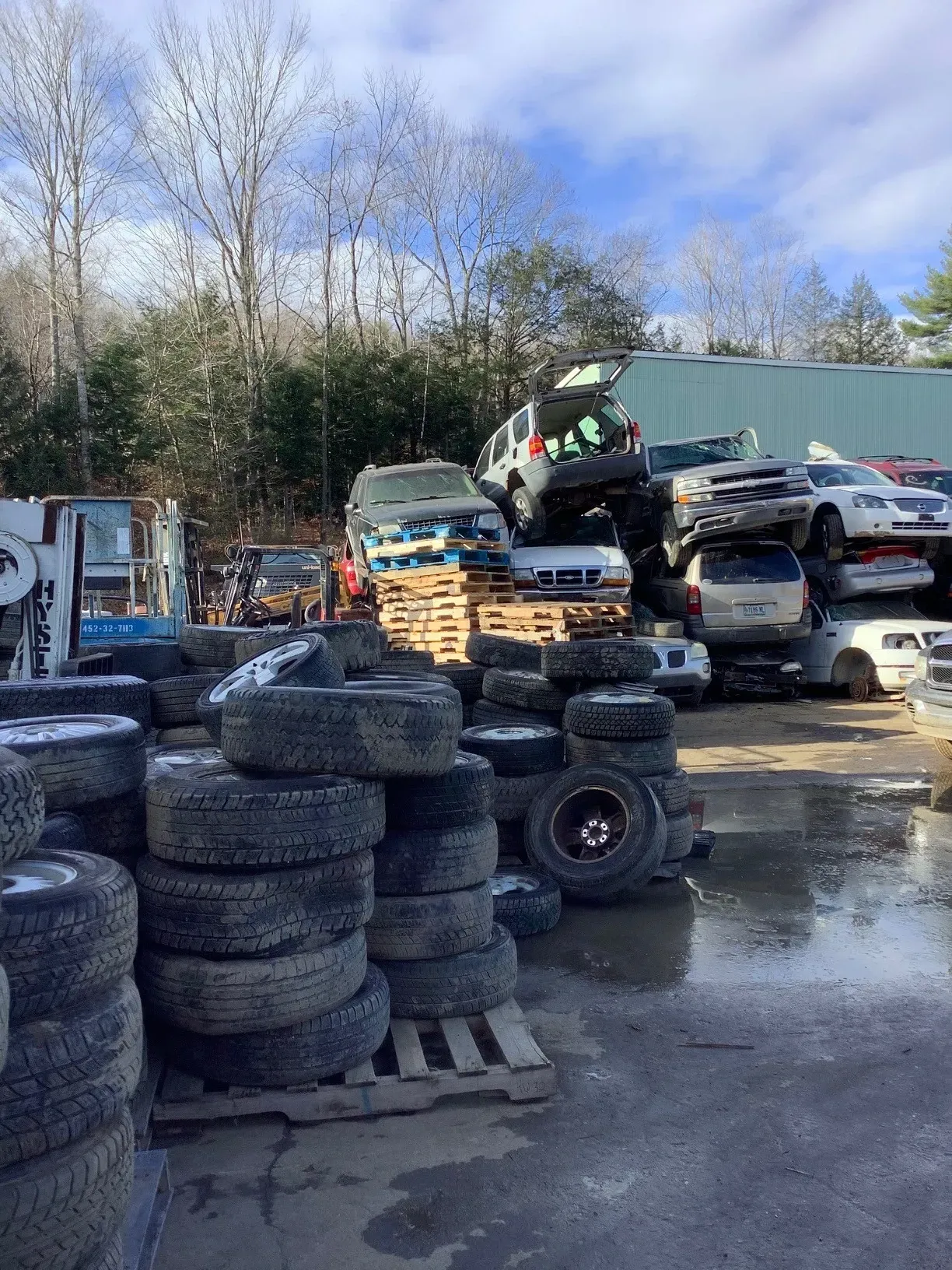 A pile of tires and cars are stacked on top of each other in a scrap yard.
