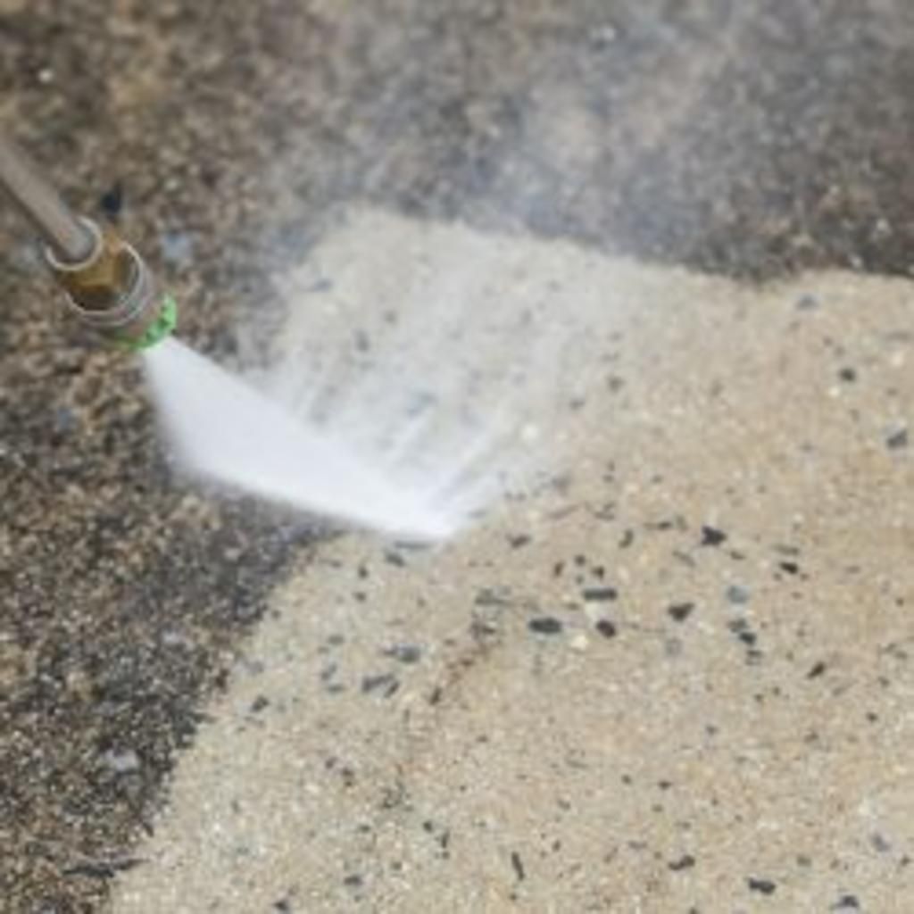 A person is using a high pressure washer to clean a concrete floor.