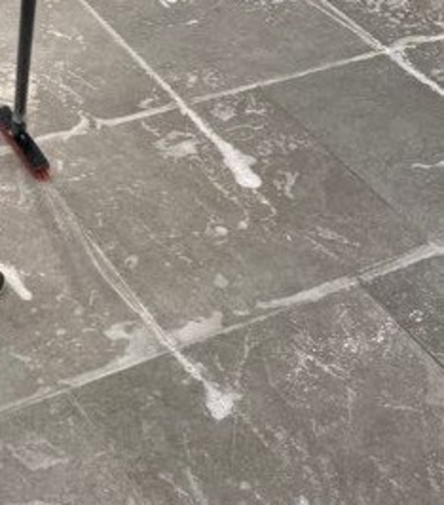 A person is cleaning a tiled floor with a broom.