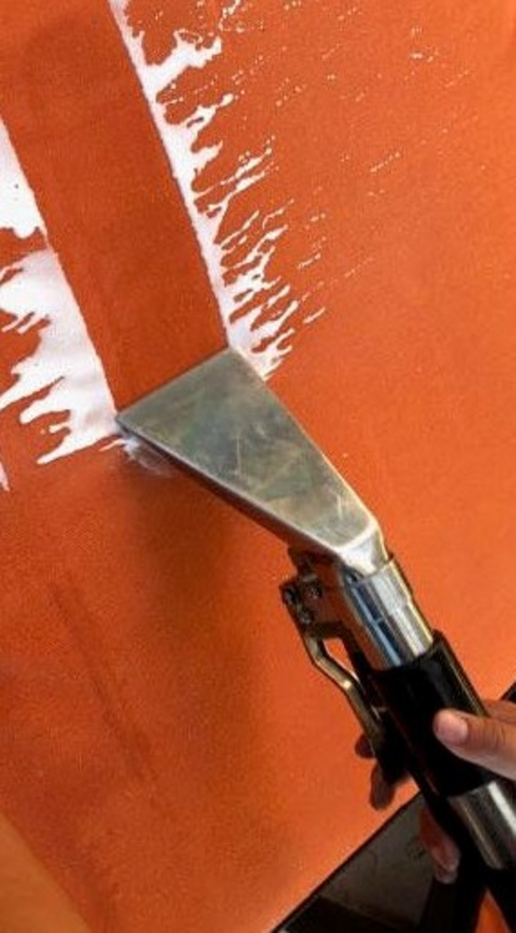 A person is using a vacuum cleaner to clean an orange surface.