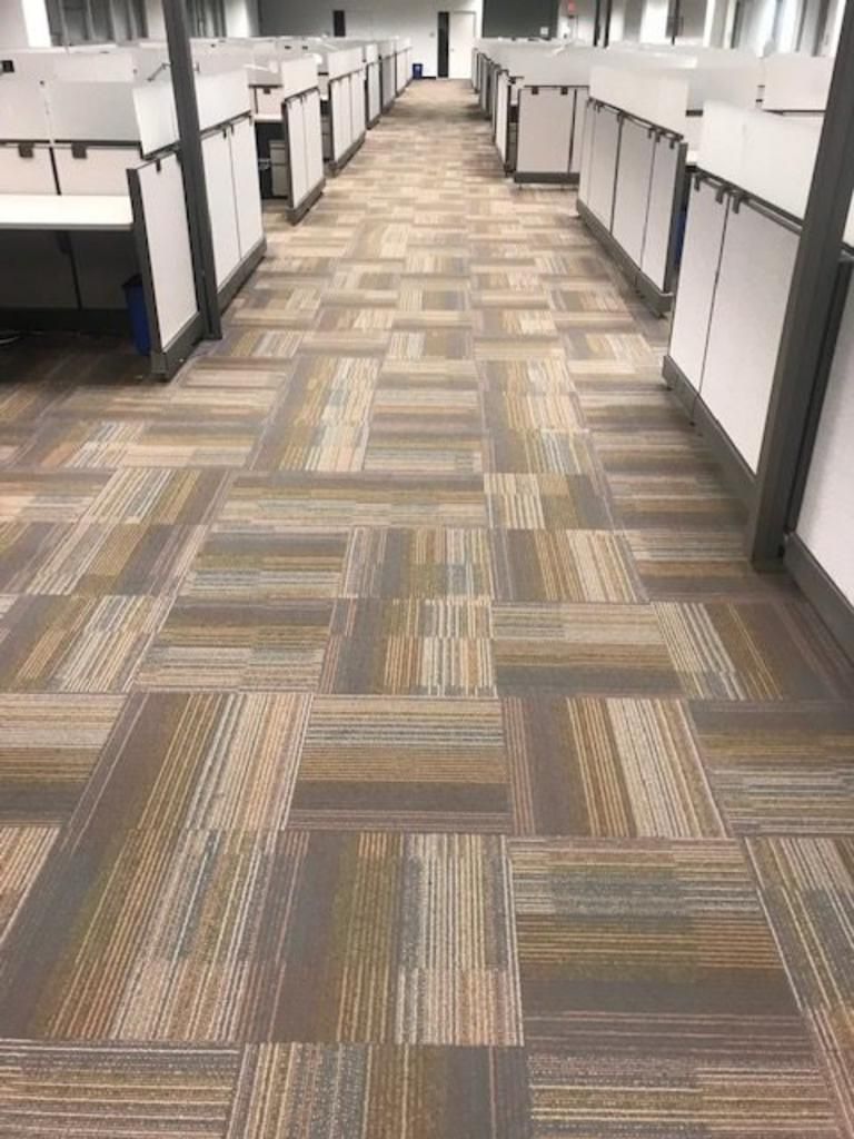 A long hallway in an office with a carpeted floor and cubicles.