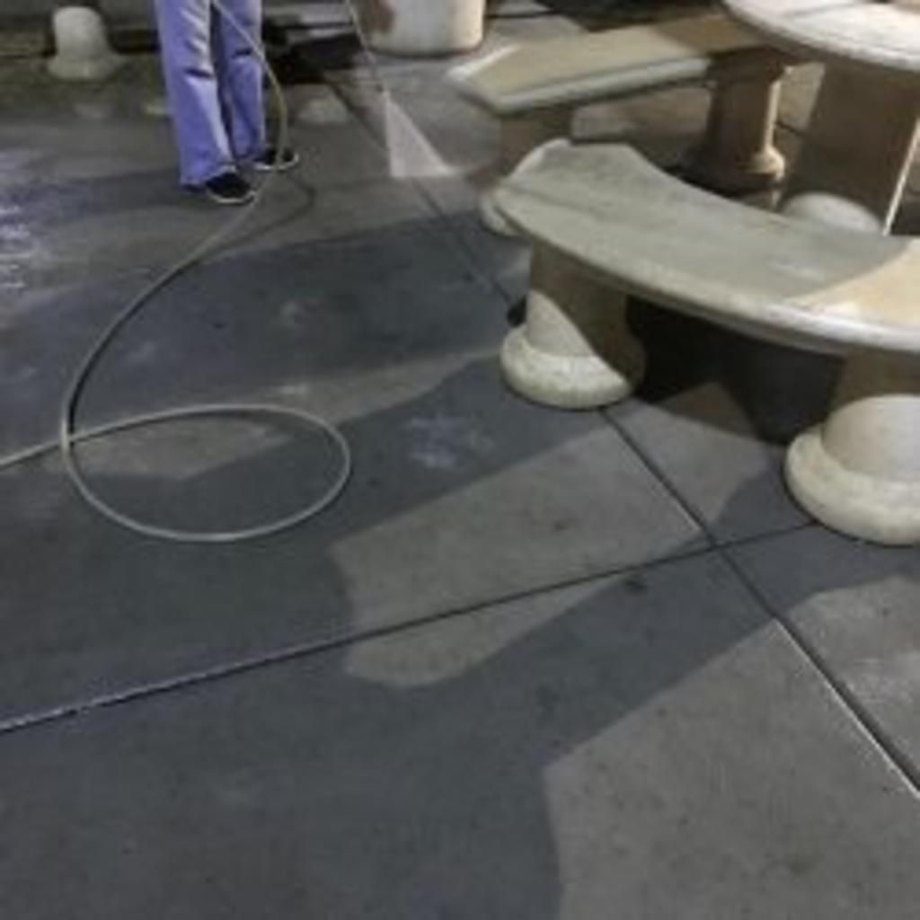 A person is cleaning a concrete floor with a hose.