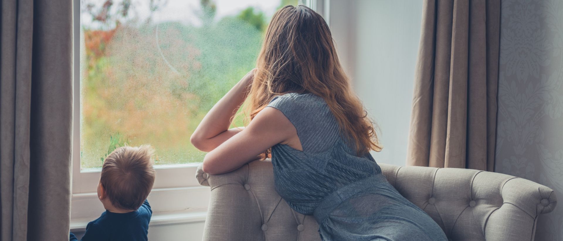 A woman and a child are sitting on a couch looking out a window.