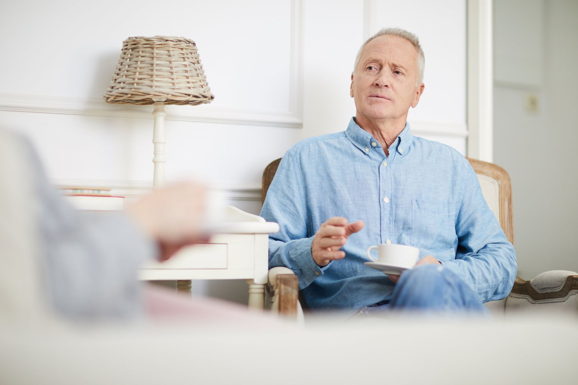 An older man is sitting in a chair drinking a cup of coffee.