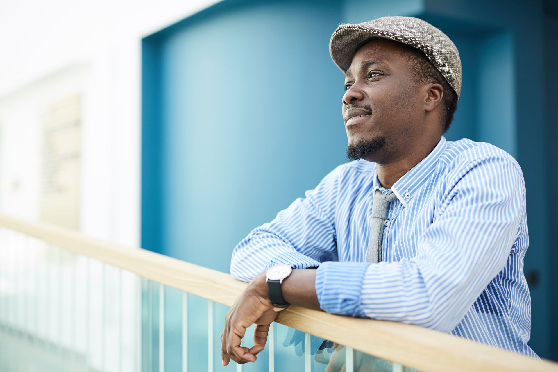 A man wearing a hat and tie is leaning on a railing.
