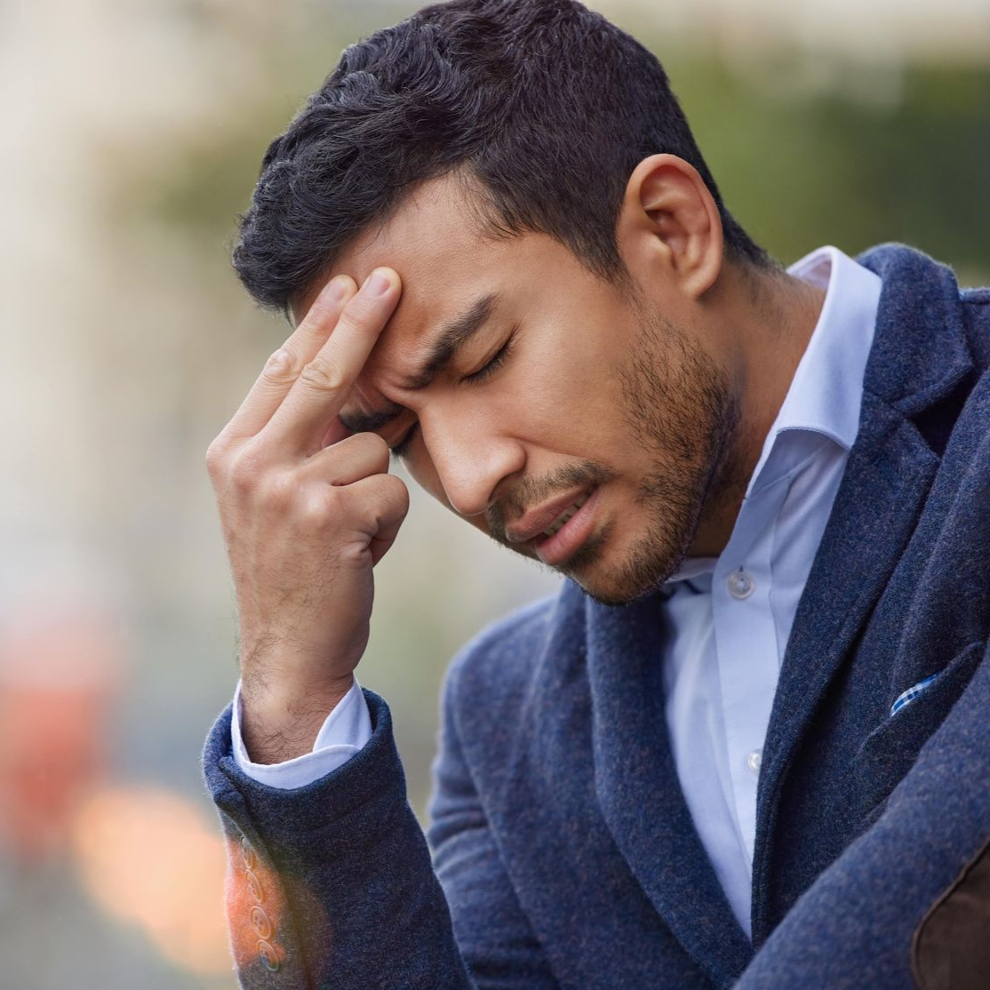 A man with a beard is standing in front of a white wall with his arms crossed and his hand on his chin.