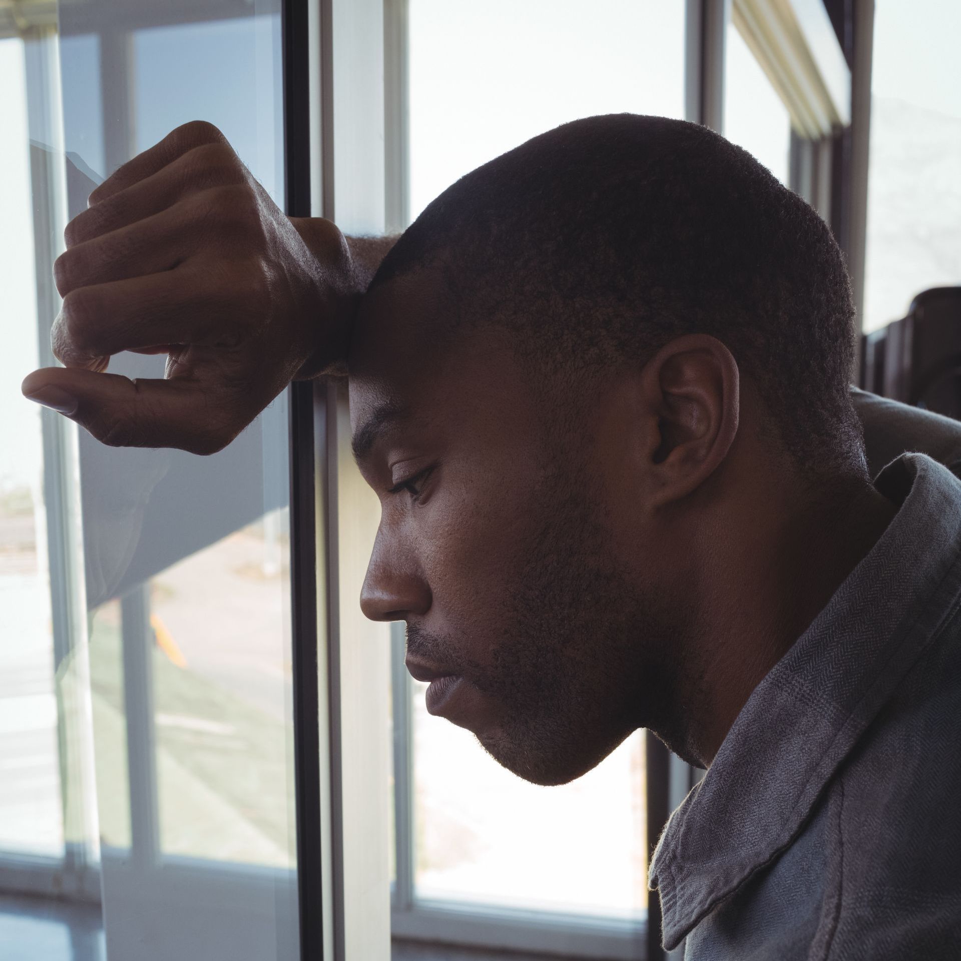 A man with his hand on his head looking out a window