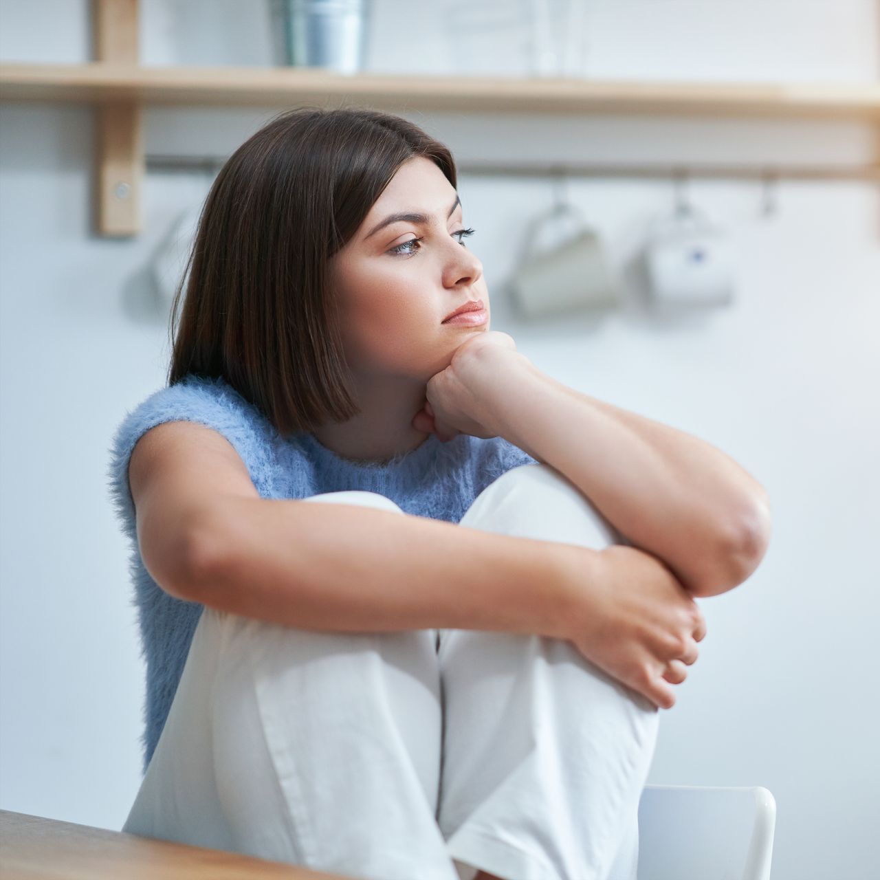 A woman is sitting at a table with her legs crossed and her head resting on her hand.