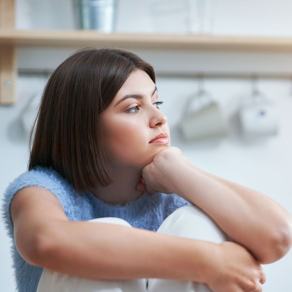 A woman is sitting on the floor in a kitchen next to a cell phone.