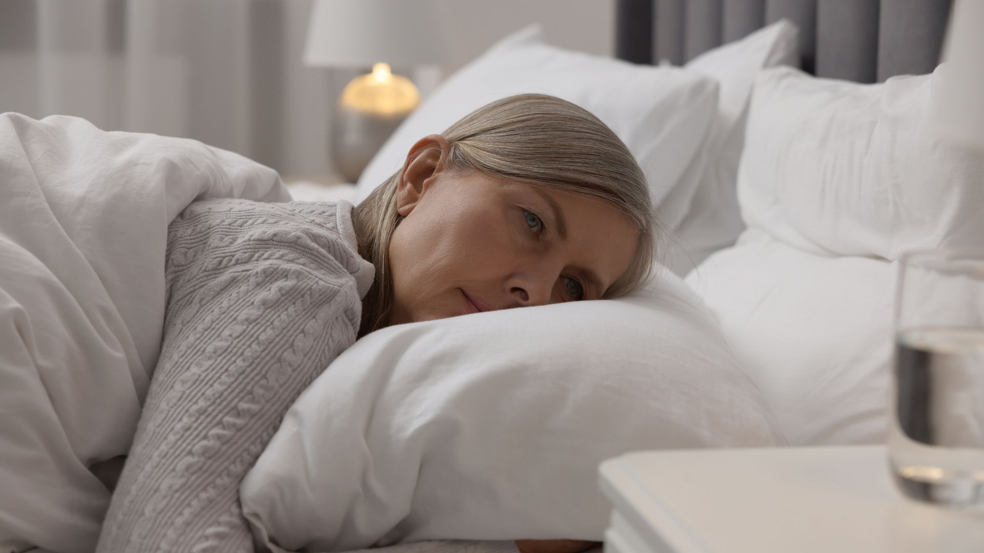 A woman is sleeping in a bed next to a glass of water.