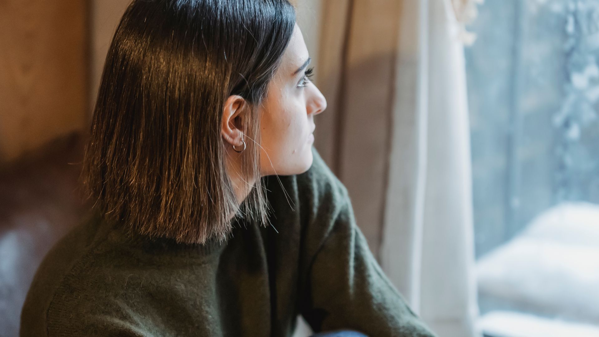 A woman in a green sweater is looking out of a window.