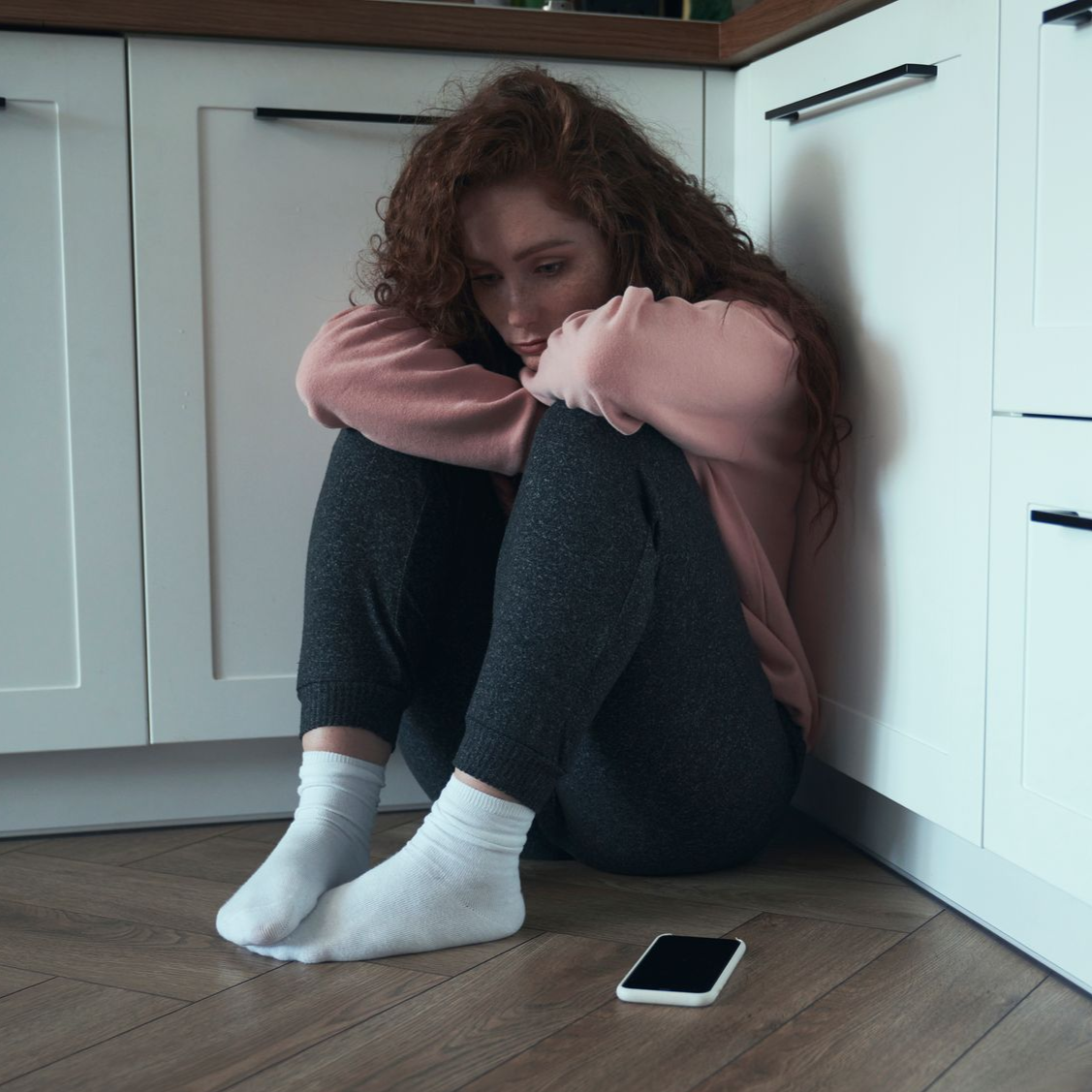 A woman is sitting on a couch with her hands on her head.