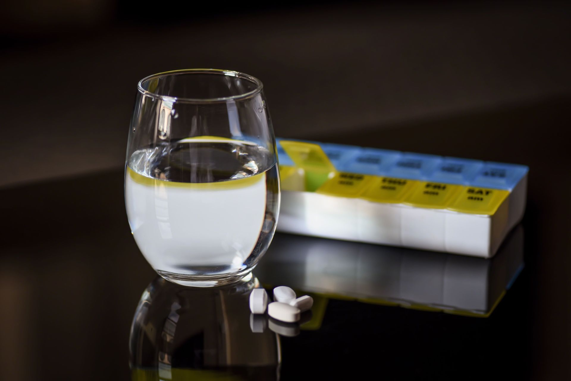 A glass of water is sitting on a table next to a box of pills.