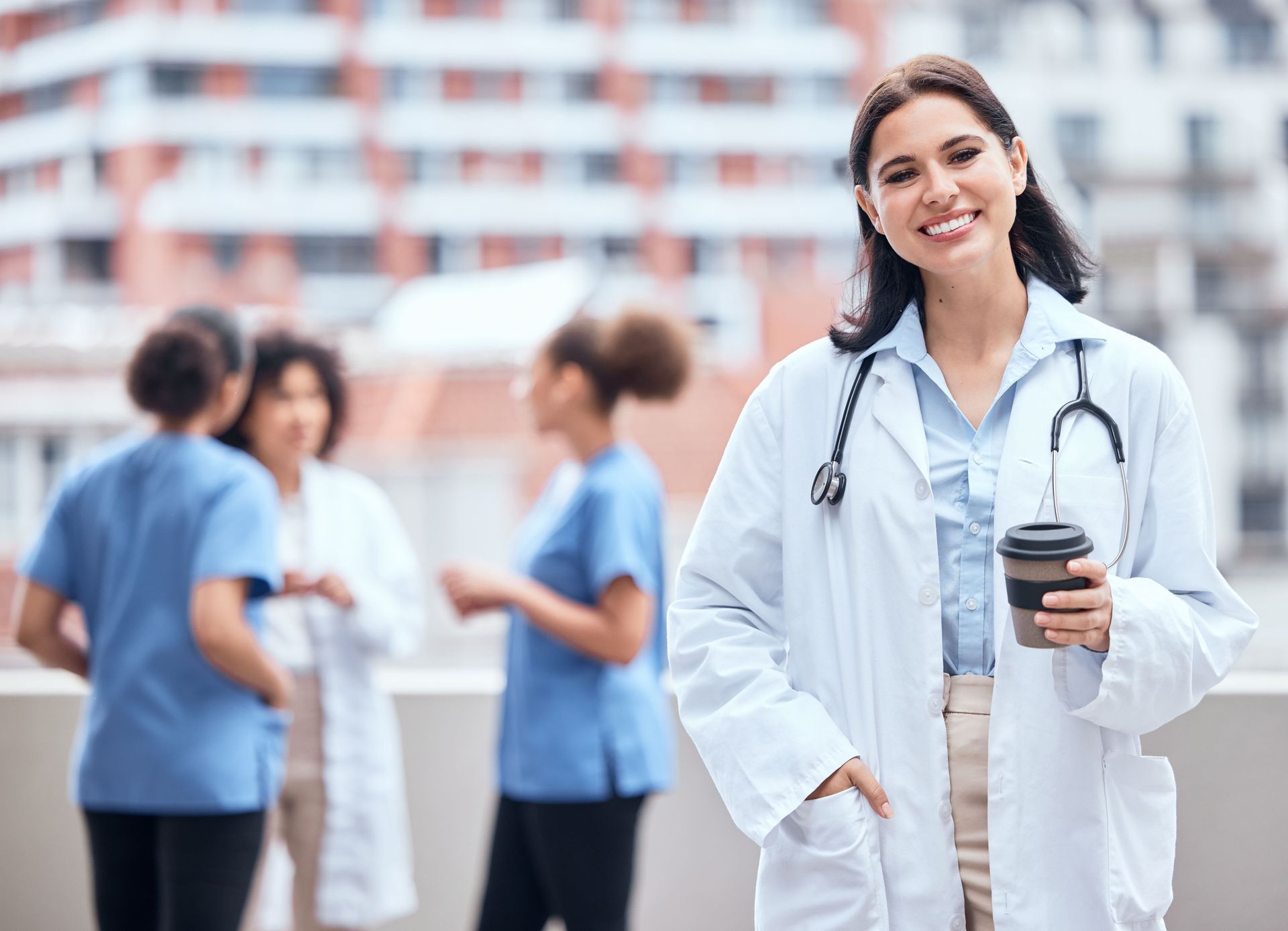 A female doctor is standing in front of a group of nurses holding a cup of coffee.