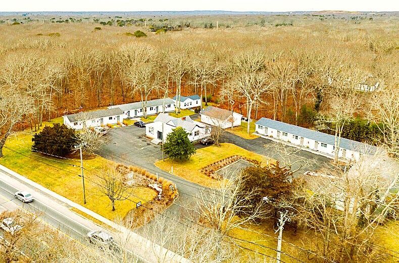 Aerial view of a motel complex surrounded by brown trees and a road with cars.