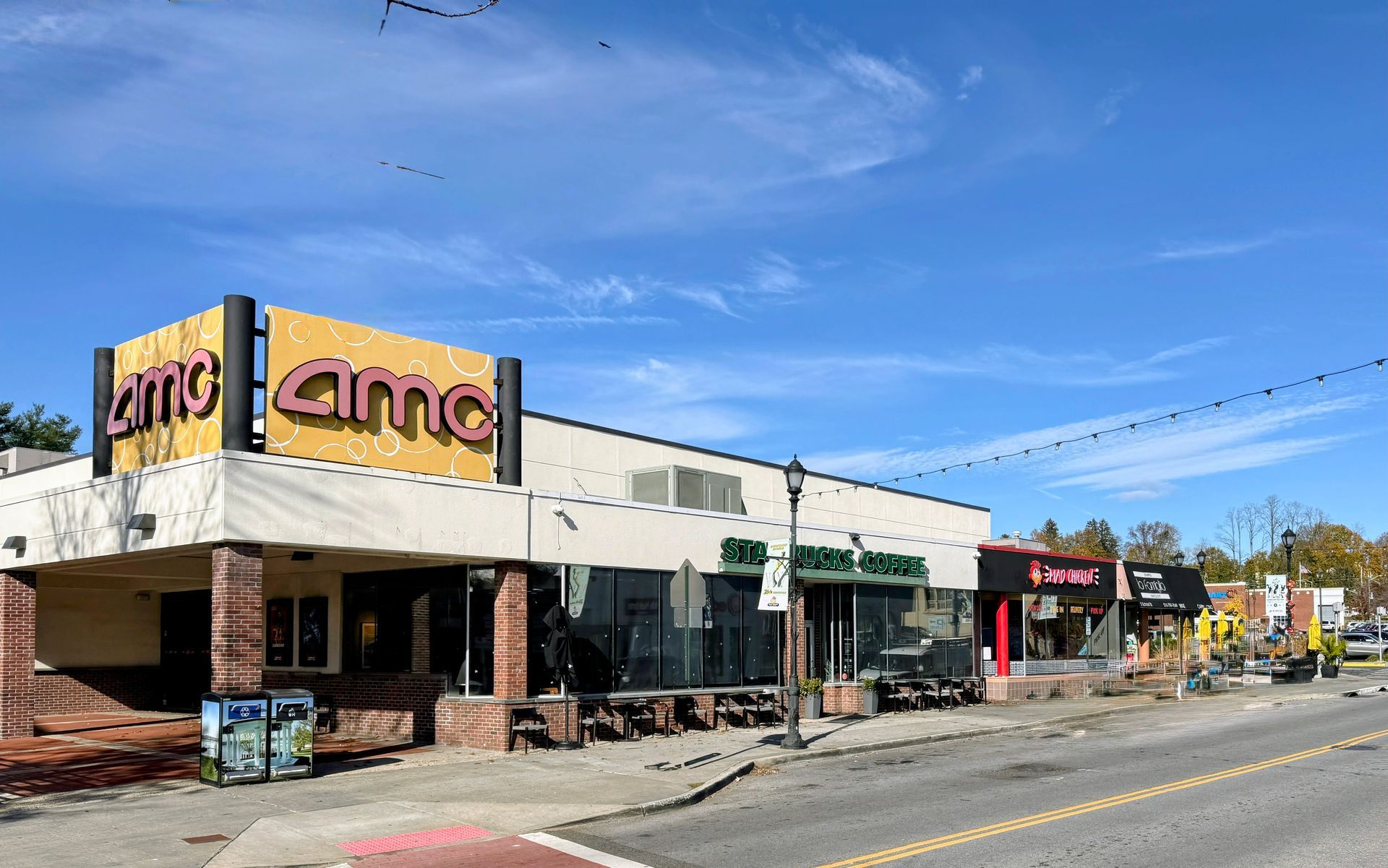 AMC movie theater and shops under a blue sky on a street.