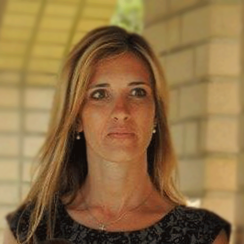 Woman with blonde hair looks toward the viewer; outdoors with a patterned top.