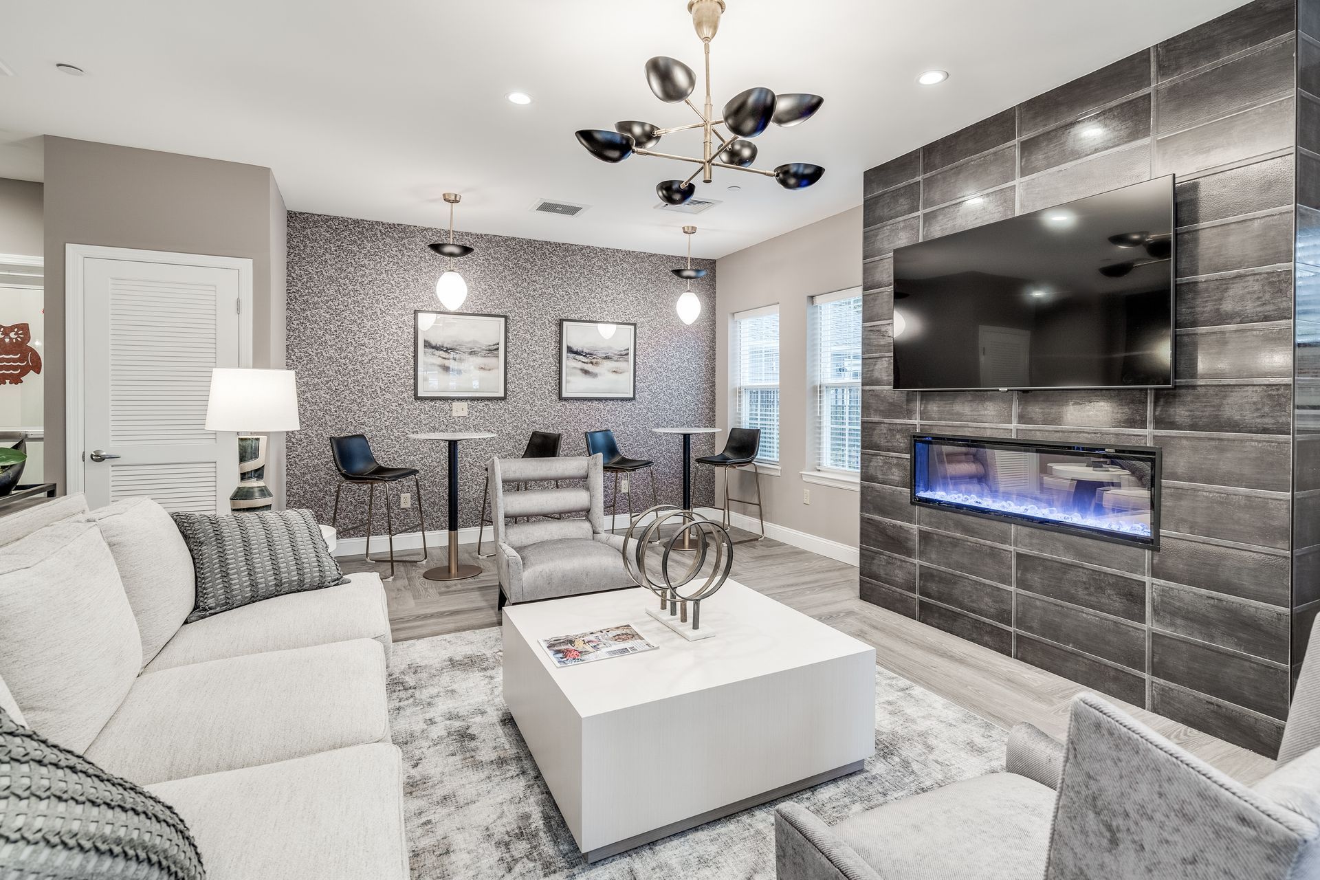 Living room with gray, textured walls, fireplace, TV, white couches, and modern chandelier.