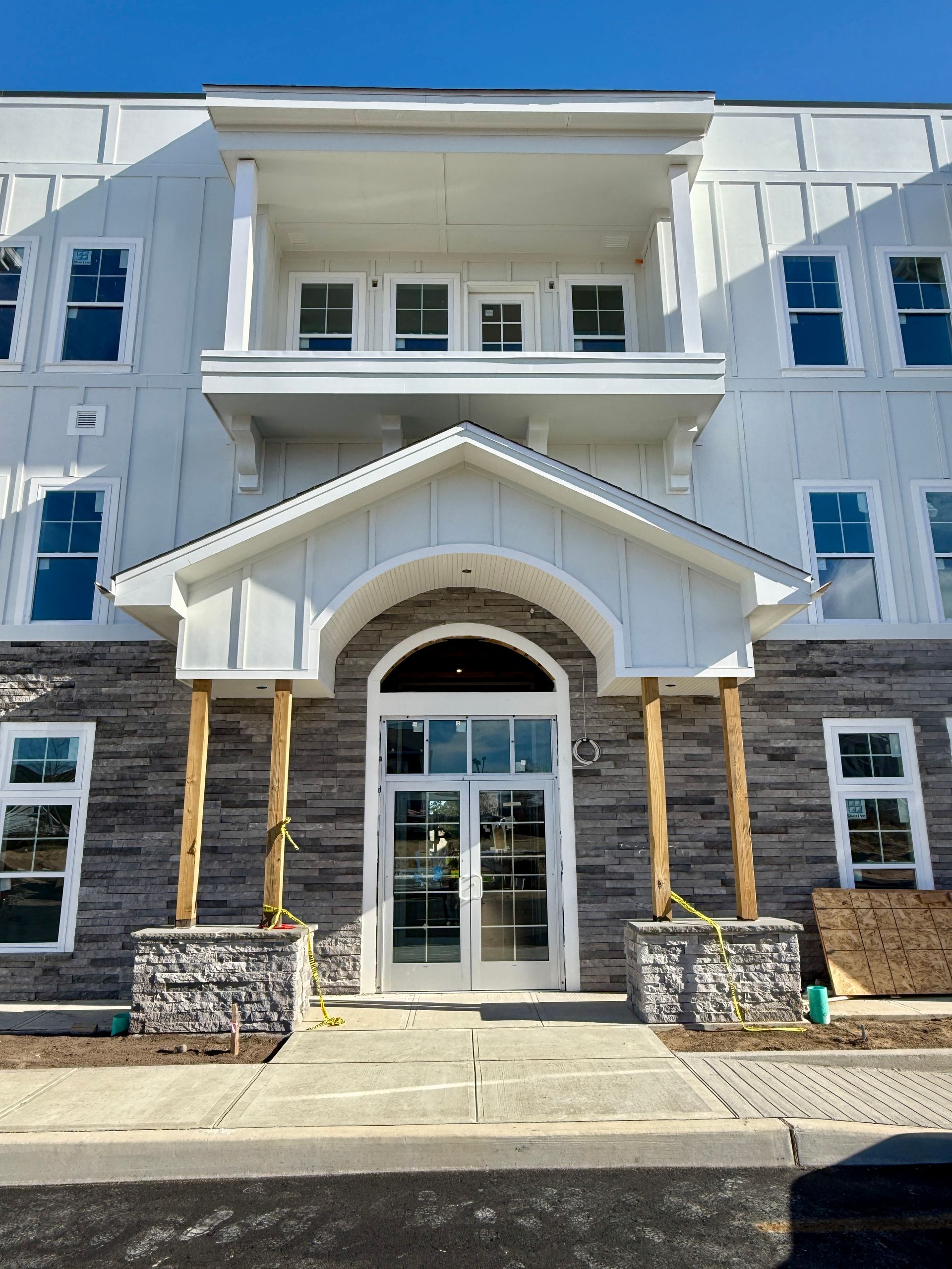 White and gray building entrance with stone accents, arched doorway, and balcony.