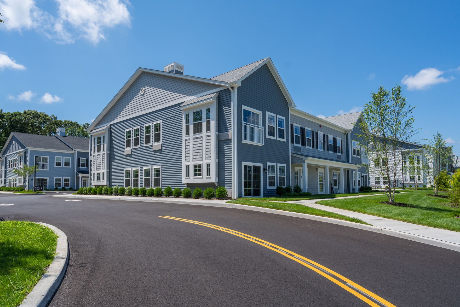 Blue multi-unit building with silver roof and driveway on a sunny day.