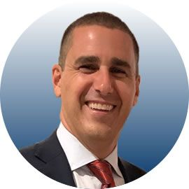 Man in suit smiling, with a red tie, against a blue and white gradient backdrop.