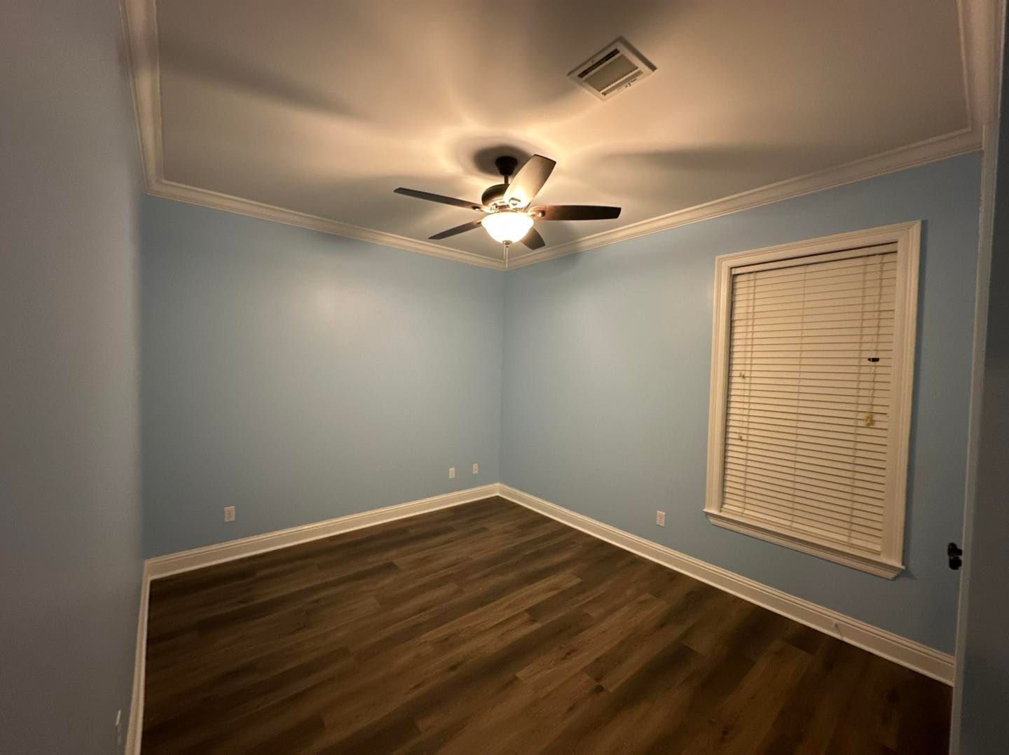 Empty light-blue bedroom with wood floor, ceiling fan, and window blinds.