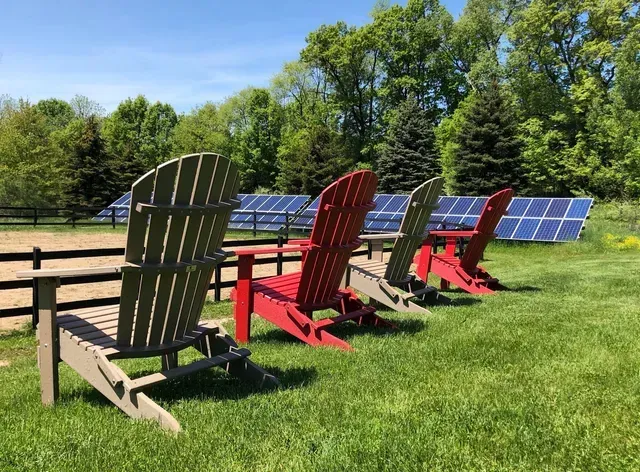 Four Adirondack chairs on grass, solar panels in background.