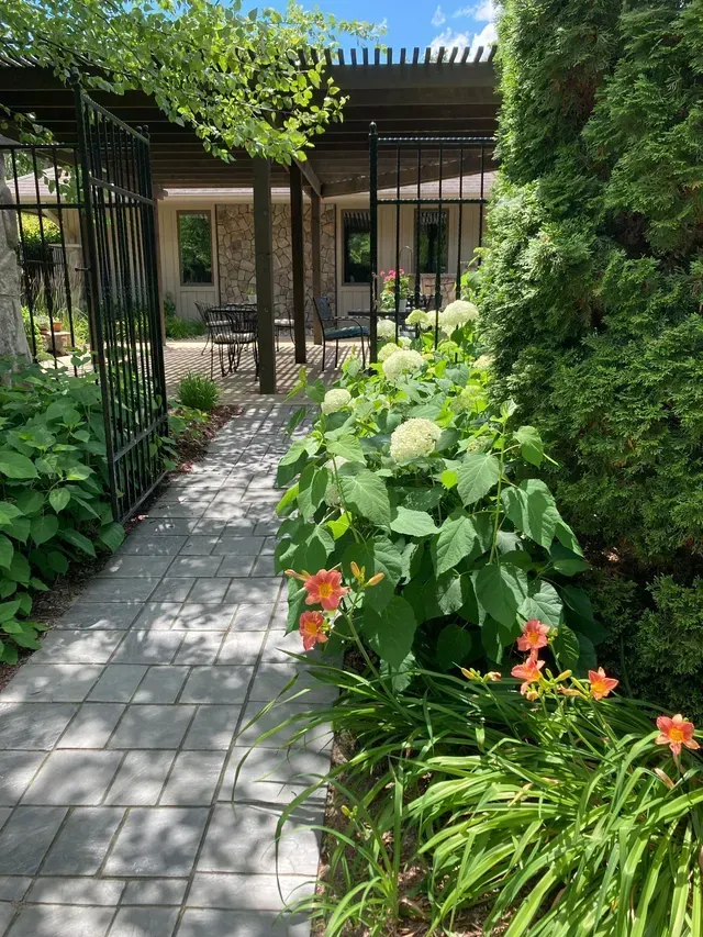 Stone path leading to a shaded patio, lined with greenery and orange flowers.