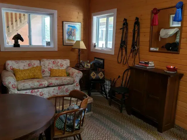 Cozy room with a floral couch, horse tack, and round table. Orange walls, windows, and wood furniture.