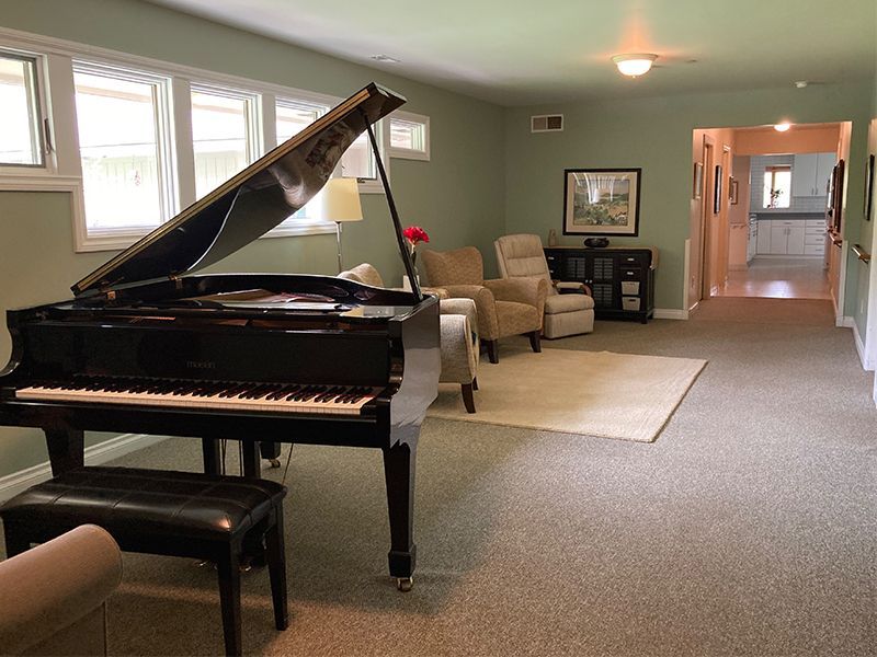 Grand piano in a living room, green walls, light carpet, two armchairs, and a doorway to another room.