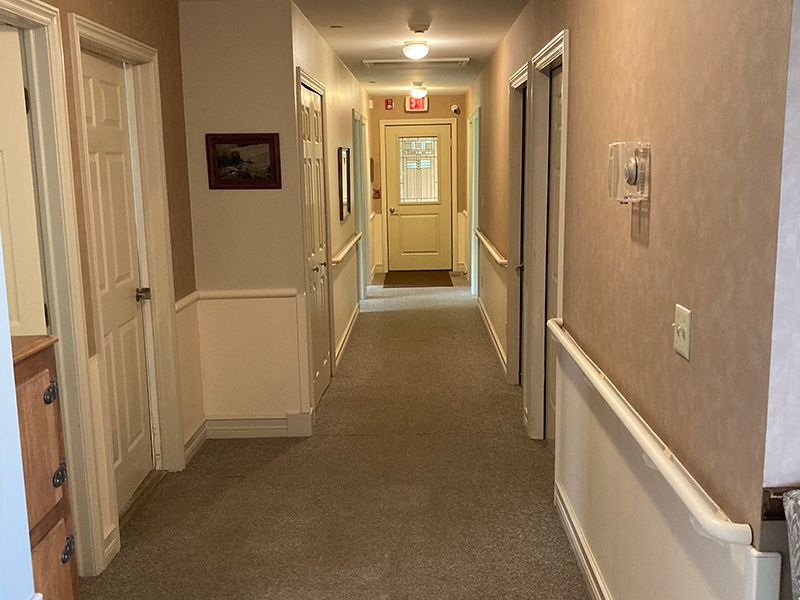 Hallway with beige walls, carpet, doors, and an exit sign.