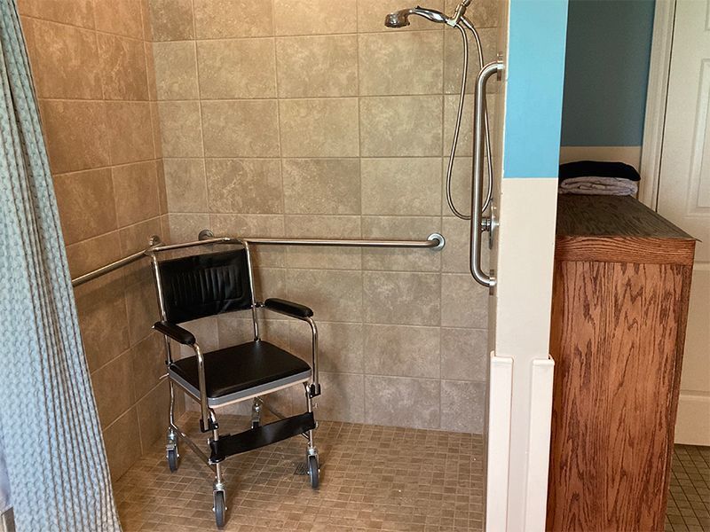 Wheelchair accessible shower with grab bars and a shower chair. Beige tiles and a partially visible curtain.