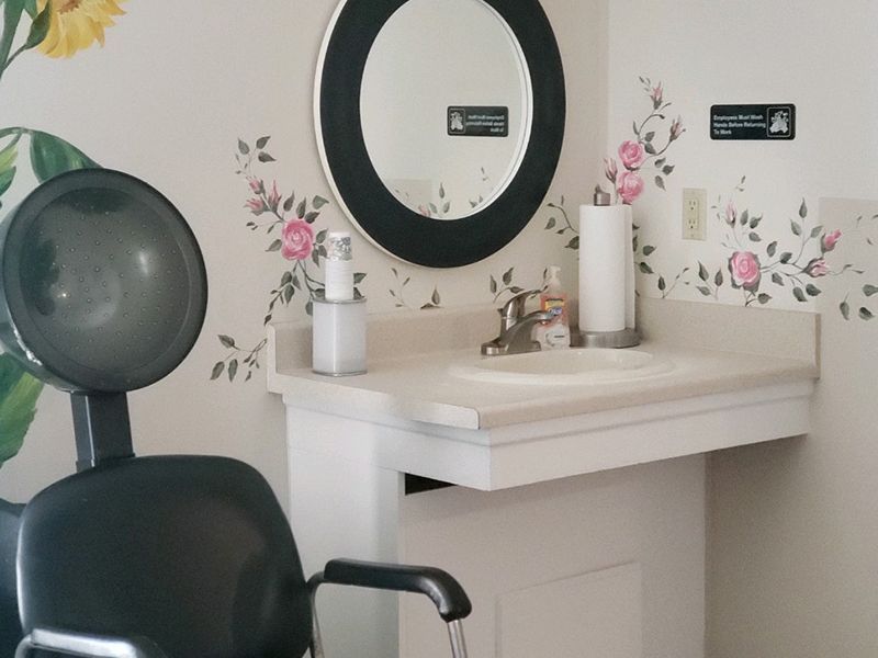 Hair salon station with sink, mirror, and dryer. Floral wall decals.