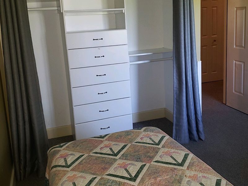 Bedroom with white closet, gray curtains, and a bed with a quilt.