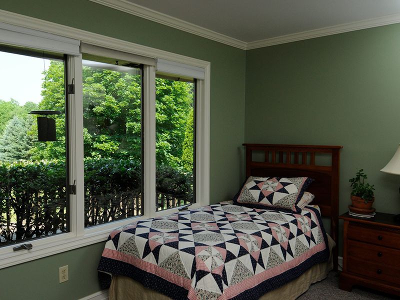 Bedroom with bed, quilt, nightstand, and window overlooking trees; green walls, white trim.